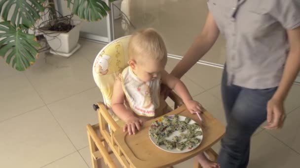 Mutter legt kleinen Sohn auf Kinderhochstuhl — Stockvideo