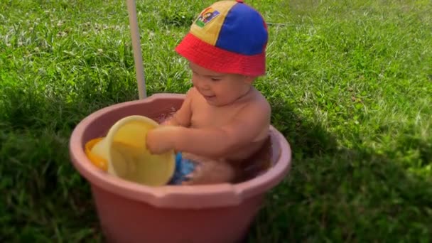 Schattig kind zwemmen in de kom met water. Dranken water uit speelgoed emmer — Stockvideo