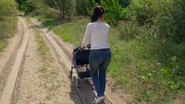 Anne bebek arabası bir Grove kumlu yolda bastırıyor