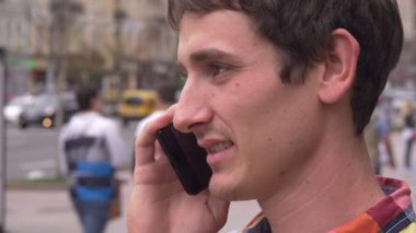 Genç adam akıllı telefonda konuşurken gökyüzüne bakar. Şehir arka plan, insanlar, arabalar