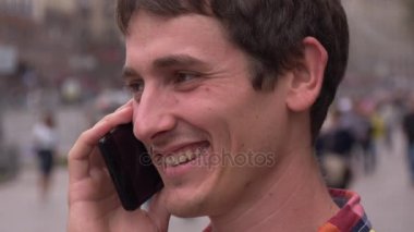 Bir cep telefonuyla konuşurken mutlu genç adam gülümsüyor. Yakın çekim. Şehir arka plan, insanlar, arabalar. Europe