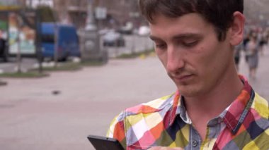 Genç adam telefon, cevaplar arama görünüyor. Şehir arka plan, insanlar, arabalar