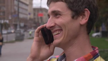 Bir cep telefonuyla konuşurken mutlu genç adam gülümsüyor. Şehir arka plan, insanlar, arabalar. Europe