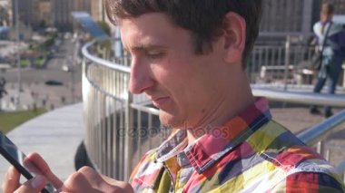 Adam manifatura, akıllı telefon kullanmaktır. Şehir arka plan, insanlar, arabalar, binalar. Güneşli yaz gün