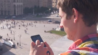 Adam akıllı telefon kullanıyor. Arka plan şehir hayatı - insanlar, arabalar, binalar üzerinde