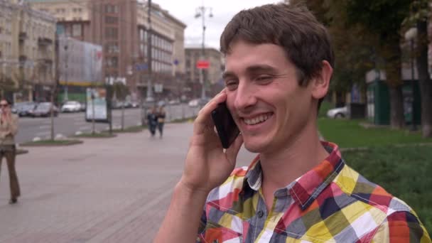 Jonge man glimlachend en praten op mobiele telefoon in centrum van stad — Stockvideo