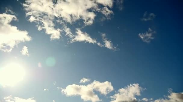 Zon beweegt op blauwe hemel. Lens flare. Sunbeam via de witte wolken. Time-lapse — Stockvideo