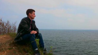 Genç adam denizin üzerinde seyir uçurumun kenarına oturur