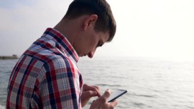 Genç adam kullanır akıllı telefon deniz kıyısında