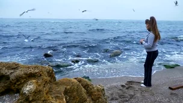 成熟した女性が海の海岸にカモメに餌 — ストック動画