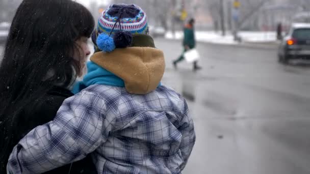 かわいい子の美しい母親は 通りを交差させます 雪片が落下します 市内の交通 — ストック動画