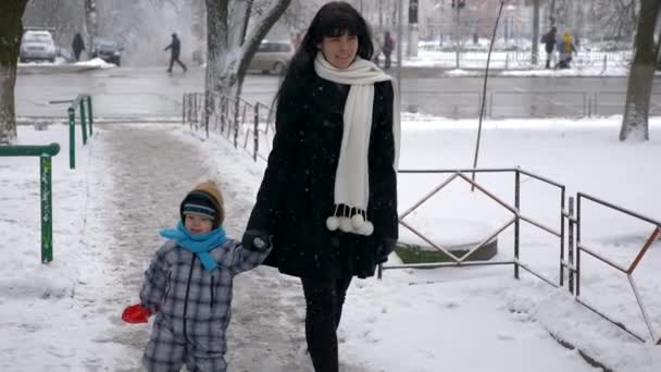若く美しい母親とかわいい子は 降雪中に屋外を歩く — ストック動画