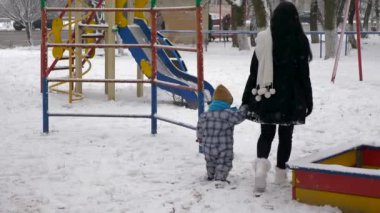 Genç güzel anne ve şirin çocuk açık havada kar yağışı sırasında oynamak. Kış City
