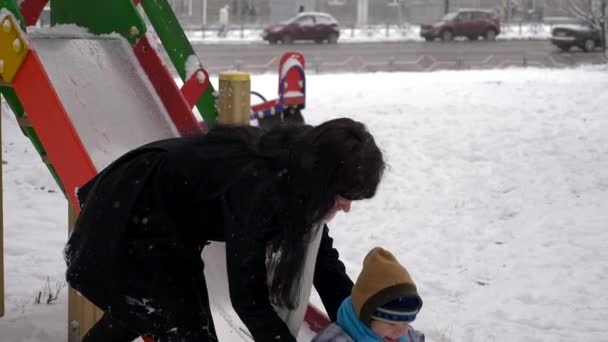 若く美しい母親とかわいい子は 降雪中に野外をプレイします — ストック動画