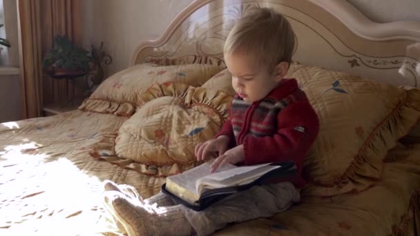 Малыш Сидит Библией Кровати Спальне Открывает Книгу Переворачивает Страницы — стоковое видео