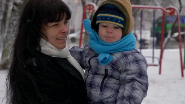 若く美しい母親とかわいい子は 降雪中に屋外を歩く — ストック動画