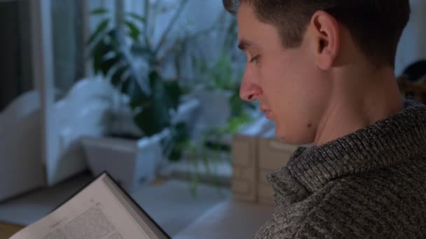 Hombre Guapo Sienta Sofá Leyendo Libro Bíblico Sala Noche Movimiento — Vídeo de stock