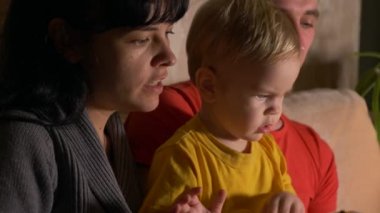 Mutlu bir aile. Genç adam ve kadın kitap okumak çocuk ile divan. Ağır çekim. Akşam Oda