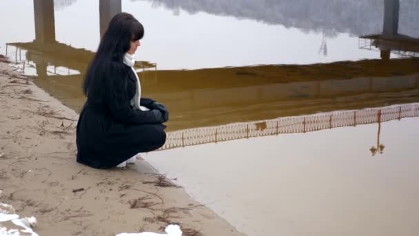 美丽的黑发人坐在河岸上思考和寻找水 慢动作冬季 — 图库视频影像
