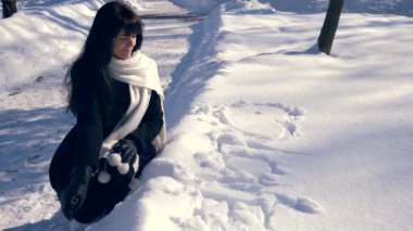 Kelime aşk ve kar üzerinde çizilmiş kalpleri yakın yalnız kız oturuyor. Winter Park güneşli bir günde. Ağır çekim 30 fps 1/2 gerçek zamanlı hız 60 fps