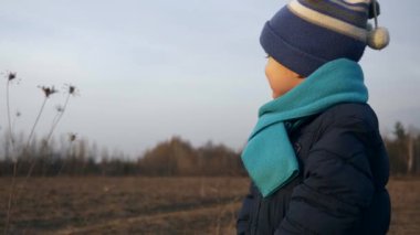 Portrait Cute Child Smiles Enjoying Nature Environment on Evening Spring/Autumn Landscape Background. Little Boy Alone in the Field Plains Watching Sunset Sky. Slow motion 0.5 speed 60fps
