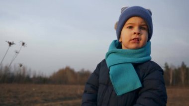 Küçük çocuk gün batımını seyreden birine bakıyor. Çocuk, sahanın ortasında durmuş, Doğanın tadını çıkarıyor. Bahar Sonbaharı Peyzajı. Yavaş çekim 0.5 hız 60fps