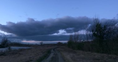  Nehir kıyısındaki kırsal yolda yürüyorum. Kırsal alan manzarası Mavi Saat Alacakaranlık Gökyüzü. Akşam Bulutları. Rüzgâr Şiddetli Bulutlar. Mevsim Değişikliği Sonbahar Bahar Zamanı.