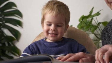 Büyük büyükannem torununun torunuyla kitap okuyor. Aktif Yaşlı Kadın, Küçük Çocuk 'la Bebek Bakıcılığı Evde Gündüz Vaktinde Bir Kitabın Sayfalarında Resimlerini Gösteriyor. Yavaş çekim 0. 5 hız 60 fps