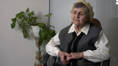 Yaşlı, üzgün, yaşlı bir kadının portresi. Yaşlı, büyük büyükannenin hayatı hakkında düşünmesi. Koltukta sakin oturması hakkında. Yavaş çekim 0. 5 hız