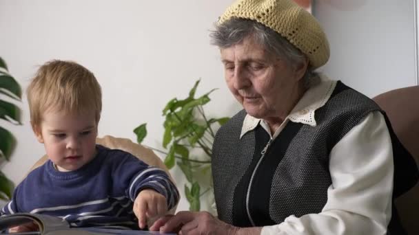 曾孫との曾祖母読書本 小さな子供が自宅で本のページに写真を表示しているアクティブ高齢女性の赤ちゃん昼間 スローモーション0 5速度60 Fps — ストック動画