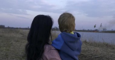 Anne ve Oğlu Kuru Çimen Ovası 'nda Yaban Ateşi' ni izliyor. Nehrin yanındaki arazide yürüyüş ve yürüyüş. Kırsalda Sabah Akşamı. Kırsal Manzara Manzarası Bahar Sezonu