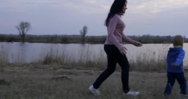 Anne ve çocuk nehir kenarındaki tarlada koşuyor. Sabah Akşam Yürüyüşü Kırsalda Yürüyüş. Bahar Zamanı Bahar Akşamı