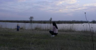 Anne ve çocuk nehir kenarındaki tarlada koşuyor. Sabah Akşam Yürüyüşü Kırsalda Yürüyüş. Bahar Zamanı Bahar Akşamı