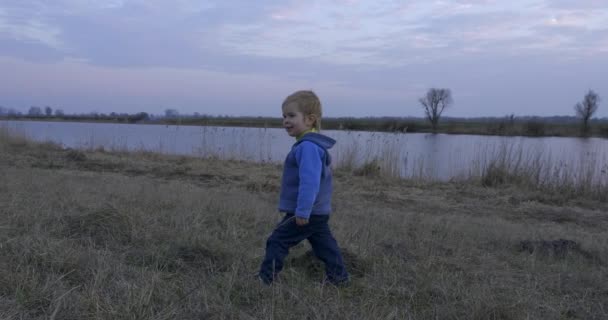 Niño Feliz Jugando Suelo Campo Hierba Cerca River Tarde Primavera — Vídeos de Stock
