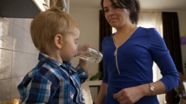 Anne, Oğul 'a bir bardak su verir. Su İçen Küçük Çocuk. Mutfak tezgahında oturan çocuk. Pencereden Sabah Akşamı Güneşi. 2x Yavaş çekim, 0.5 hız 60 FPS