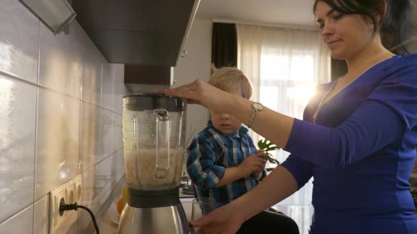 母子俩在搅拌机里用发芽的小麦酿制水果鸡尾酒 小孩坐在厨房台面上 晨光透过窗户照进来 2X慢动作 5速度60 Fps — 图库视频影像