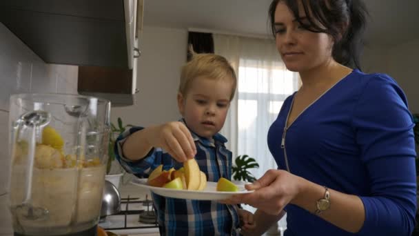 小儿子帮妈妈做饭 为她做饭 小孩在搅拌机里放苹果片 小孩坐在厨房台面上 晨光透过窗户照进来 2X慢动作 5速度60 Fps — 图库视频影像