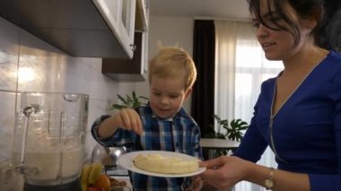 Küçük Oğlu, Anne 'nin Yemek Hazırlamasına Yardım Ediyor. Çocuk, muz parçalarını karıştırıcıya koyar. Mutfak tezgahında oturan çocuk. Pencereden Sabah Akşamı Güneşi. 2x Yavaş çekim, 0.5 hız 60 FPS