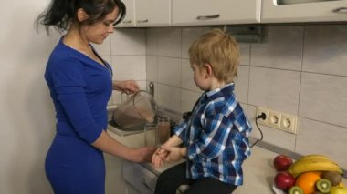 Kadın bardağa meyve kokteyli dolduruyor. Anne ve Oğul Mutfakta Yemek Hazırlıyor. Mutfak tezgahında oturan çocuk. Pencereden Sabah Akşamı Güneşi. 2x Yavaş çekim, 0.5 hız 60 FPS