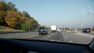Şehir Otobanı boyunca giden araba. Ön cam Ön ekran Başlıklı Kız Görünümü. Ukrayna Kyiv 2018. Parlak güneşli yaz sonbahar sabahı, mavi gökyüzü. 2x Yavaş çekim 0. 5 hız 60 FPS