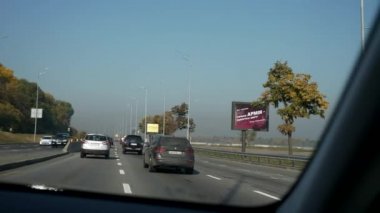 Şehir Otobanı boyunca giden araba. Ukrayna Kyiv 2018. Ön cam Ön ekran Başlıklı Kız Görünümü. Parlak güneşli yaz sonbahar sabahı, mavi gökyüzü. 2x Yavaş çekim 0. 5 hız 60 FPS