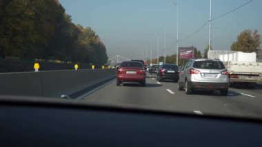 Şehir Otobanı 'nda trafik sıkışıklığında araba hareket ediyor. Ön cam kaput görüntüsü. Arabalar şehir caddesinde hareket ediyor. Ukrayna Kyiv 2018. Parlak güneşli yaz sonbahar sabahı, mavi gökyüzü. 2x Yavaş çekim 0. 5 hız 60 FPS