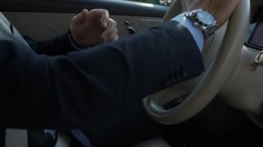 Yakın plan erkek elleri lüks birinci sınıf lüks arabanın direksiyonunu çeviriyor. Mercedes-Benz S sınıfı. Genç Başarılı Beyaz İş Adamı Şehir Caddesinde, Şehir Otobanı 'nda Kendine Güvenen Sürücü. Parlak Güneşli Yaz Sonbahar Sabahı.