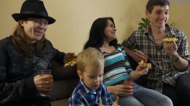 60P子供と友達と幸せな家族がパーティーをしていますトマトジュースでピザを食べる部屋のソファに座って — ストック動画