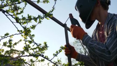 Arka bahçede Genç Kaynak Metal İnşaat. Koruyucu Miğferde çalışan bir işçi. Kırsal kesimdeki kır evinin yanındaki bahçe. 4K 2x Yavaş çekim 0. 5 x 60 FPS 