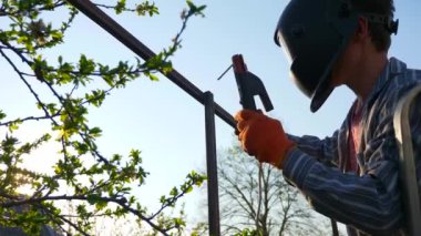 Arka bahçede Genç Kaynak Metal İnşaat. Koruyucu Miğferde çalışan bir işçi. Kırsal kesimdeki kır evinin yanındaki bahçe. 4K 2x Yavaş çekim 0. 5 x 60 FPS 