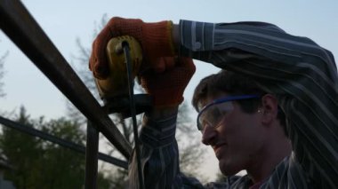 Demir Metal İnşaatını Angle Grinder ile Arka Bahçe 'de Kesen Genç Adam. Kırsal kesimde bir ev. Kırsal bölgede bir bahar akşamı. 4K 2x Yavaş çekim 0. 5 x 60 FPS 