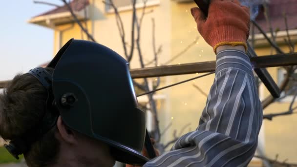 裏庭で若い男溶接金属建設 保護ヘルメットの労働者 田舎のコテージハウスの近くの庭 2Xスローモーション0 Fps — ストック動画