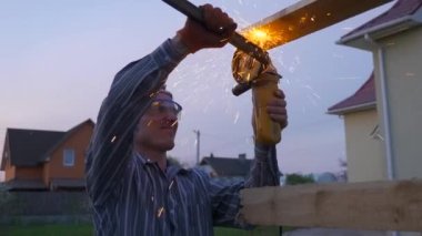 Demir Metal İnşaatını Angle Grinder ile Arka Bahçe 'de Kesen Genç Adam. Kırsal kesimde bir ev. Kırsal Bölgede Bahar Akşamı