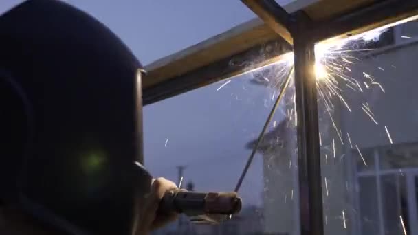 裏庭で若い男溶接金属建設 保護ヘルメットの労働者 田舎のコテージハウスの近くの庭 10ビット ハイブリッド Gama Hlg Hdr — ストック動画